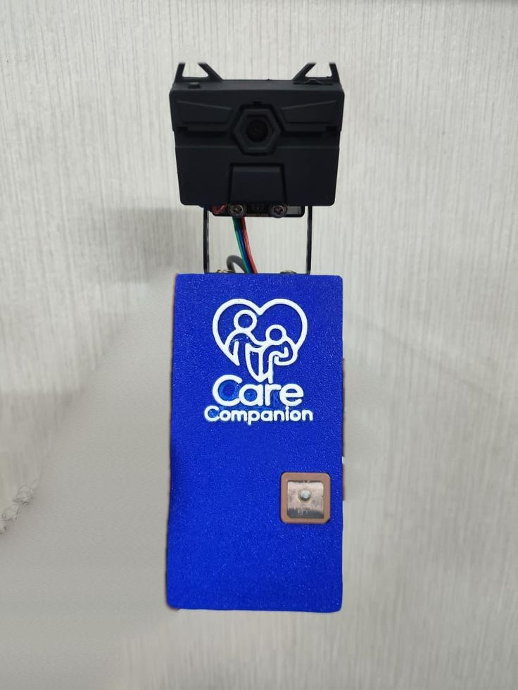 The front face of the enclosure, carrying the team's CareCompanion logo, held in hand, with the HuskyLens camera mounted above on its bracket.