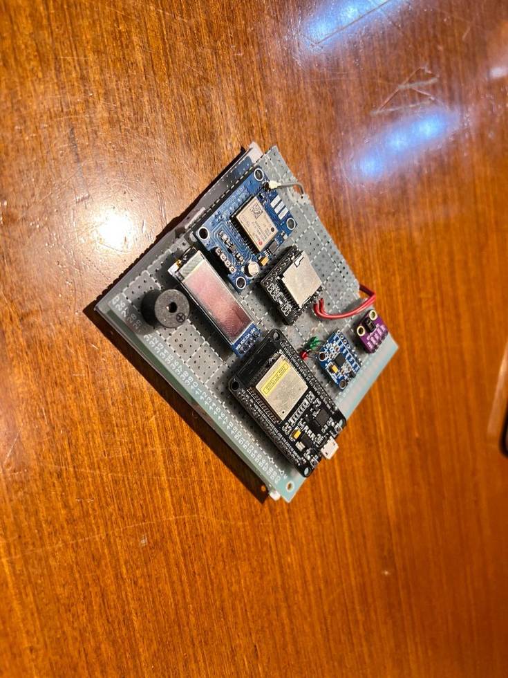 An earlier prototype: an OLED display, ESP32, SIM800L module and a buzzer wired together on a sheet of perfboard, no enclosure yet.